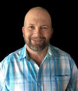 Colorado Mountain Property and Homes for Sale - A smiling man named Mitch Sample with a beard, wearing a blue plaid shirt, against a black background.