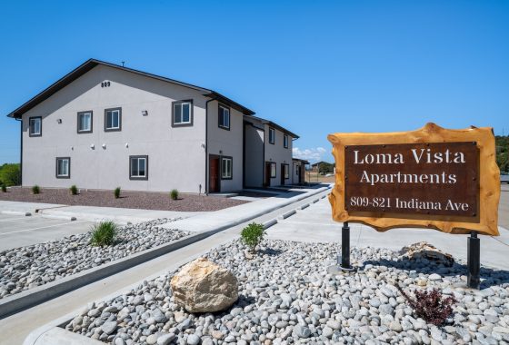 Colorado Mountain Property and Homes for Sale - A modern, two-story apartment building with a wooden sign in front reading "Loma Vista Apartments, 809-821 Indiana Ave." offers units for rent. The area is landscaped with rocks and small plants under a clear blue sky.